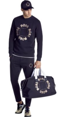 Man in black sweatshirt, black pants, and black hat by BOSS menswear