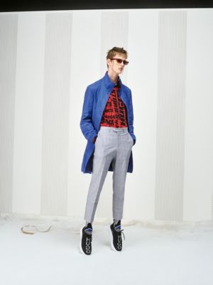 Male model wearing a blue coat, a red shirt with print, light grey trousers, black sneakers and glasses by HUGO