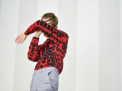 Male model wearing a red knitwear with print and light grey trousers by HUGO