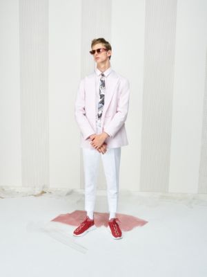 Male model wearing a pink blazer, pink shirt, tie in a print pattern, white trousers, red trainers and glasses by HUGO