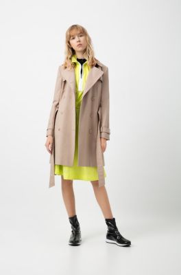 Female model wearing a beige trench coat, bright yellow dress, black T-Shirt and black trainers by HUGO