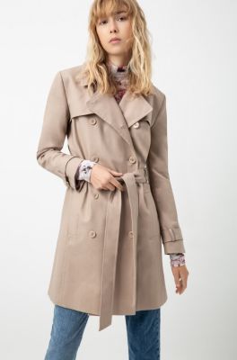 Female model wearing a beige trench coat, pink shirt with flower print and blue denim jeans by HUGO