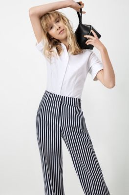 Female model wearing a white shirt, trousers with stripes and a black bag by HUGO