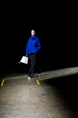 Woman on the runway wearing a blue heavy knitwear turtle neck styled with black trousers, white shoes and a white bag