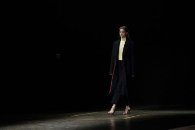 Woman wearing a white top and black trousers styled with a long dark grey coat from the BOSS Womenswear Gallery Collection