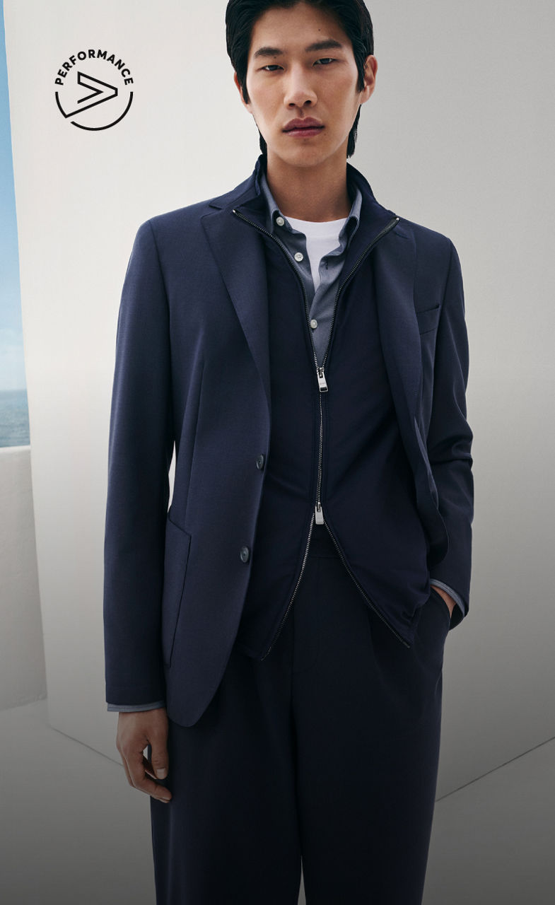 ネイビーブルーでまとめた、BOSSパフォーマンスのニットジャケット、薄手のジャケット、揃いのパンツを身に着けた男性モデル。
