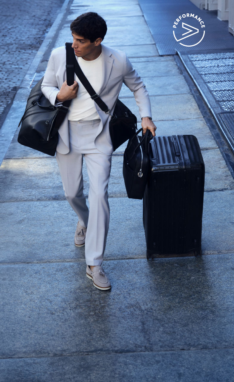 male model in the new BOSS Performance tracksuit and a baseball cap all in navy blue leaning on a suitcase and a travelling bag.
