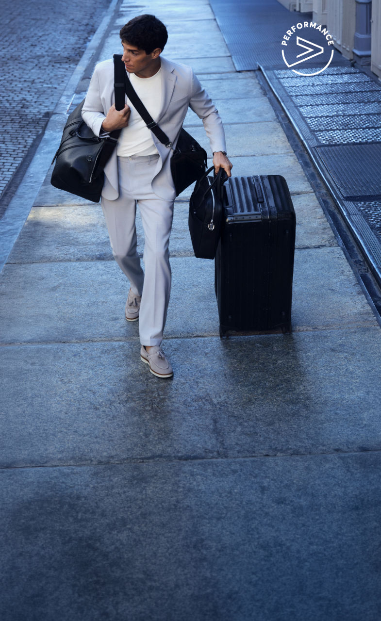 male model in the new BOSS Performance tracksuit and a baseball cap all in navy blue leaning on a suitcase and a travelling bag.